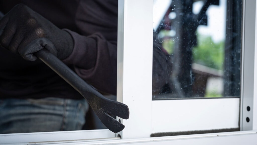 Ein Einbrecher stimmt ein Fenster mit einem Brecheisen auf